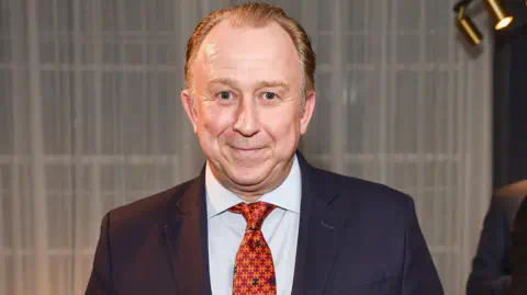 Shutterstock Nigel Blow wearing a blue suit and orange tie at the opening of the Turnbull and Asser store in Mayfair, 2015